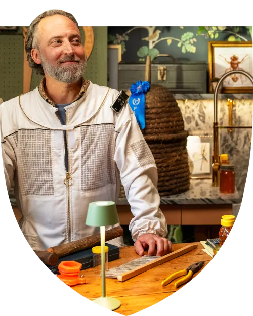 Man in beekeeper suit standing proudly at his desk